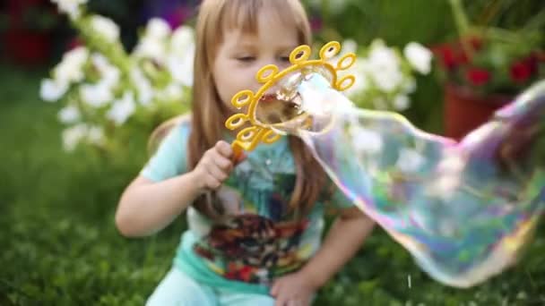 Super linda niña de pelo justo en camiseta soplando burbujas de jabón en la hierba . — Vídeo de stock
