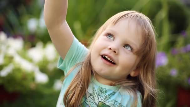 Σούπερ χαριτωμένο ξανθό μικρό κορίτσι στο t-shirt φυσώντας φυσαλίδες σαπούνι στο γρασίδι. — Αρχείο Βίντεο