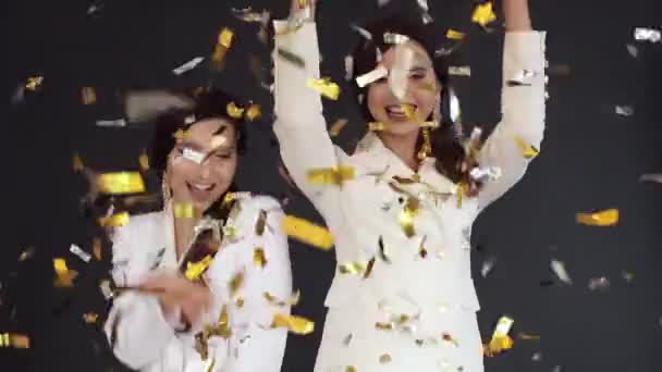 Prachtige tweeling zusters in elegante witte kostuums met plezier met confetti. — Stockvideo