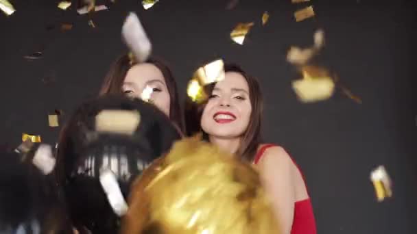 Mooie tweeling in rode en zwarte jurken met plezier met lucht ballonnen spuiten met confetti. — Stockvideo