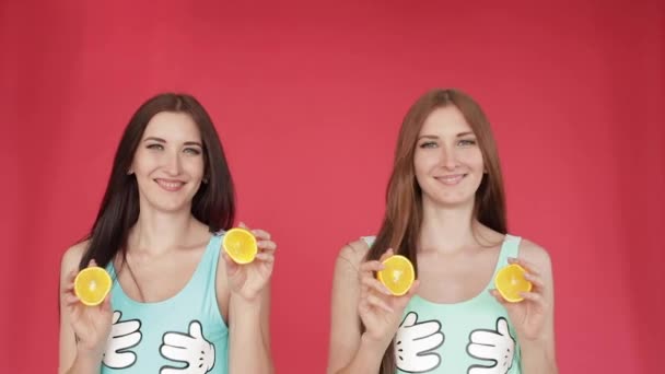 幸せな姉妹は手を出してオレンジで遊ぶ。明るいプロモーションビデオ。オレンジと赤い背景のブルネット — ストック動画