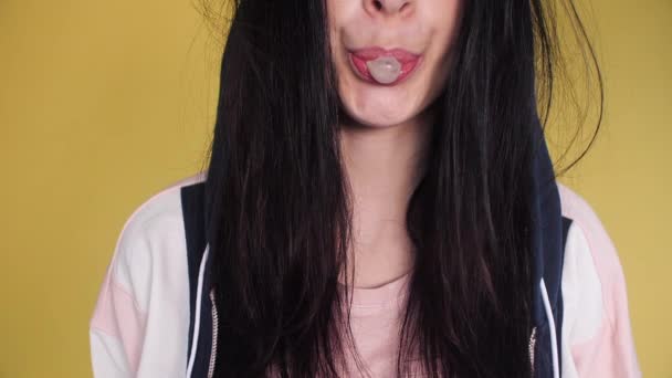 Красива дівчина з брудним волоссям, що дме жувальну гумку на жовтому фоні . — стокове відео