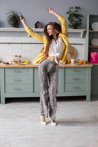 Стильна щаслива дівчина брюнетка в змії друковані штани танцюють на кухні . — стокове фото