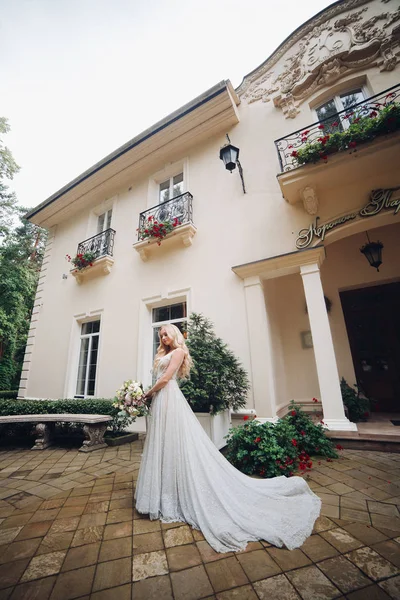 Noiva em vestido de casamento perfeito posando contra casa de luxo com boquete de casamento . — Fotografia de Stock