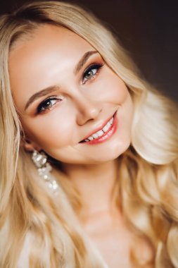 Sedactive ve çekici sarışın makyaj giyen ve kamera gülümseyen.