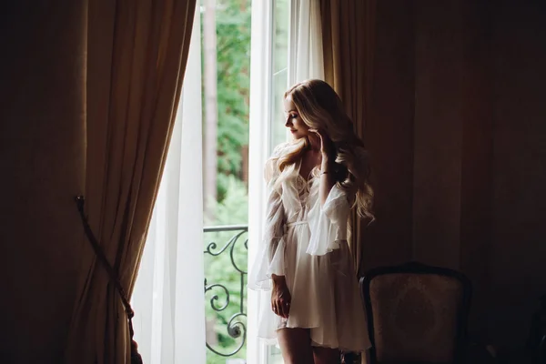 Wunderschöne Braut steht in der Nähe des Balkons und schaut in das große Fenster. — Stockfoto
