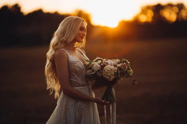 Romantisk brud Holding bröllop boquet, poserar vid solnedgången tid. — Stockfoto