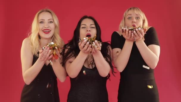 Três mulheres em vestidos pretos soprando confete em estúdio — Vídeo de Stock