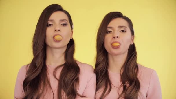 Twin girls blowing chewing gum into bubbles. — 图库视频影像