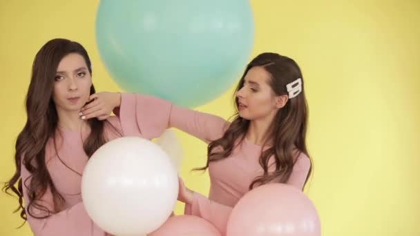 Bonitas gemelas en vestidos rosados jugando con globos de colores — Vídeos de Stock