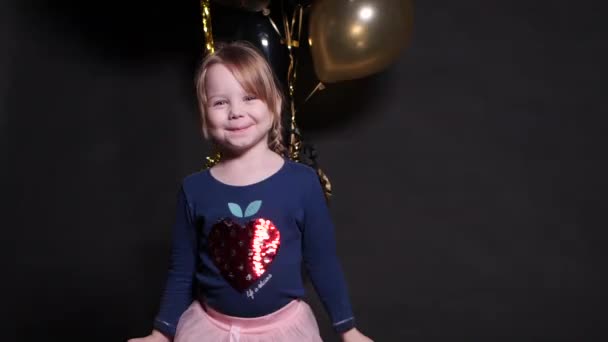 Mooie gelukkige kleine meid springen met confetti en lucht ballonnen in de achtergrond. — Stockvideo