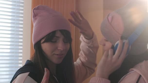 两个活跃在帽子和耳机的姐妹听音乐 — 图库视频影像