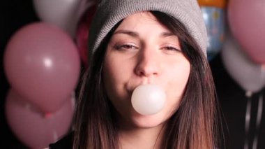 Gri şapkalı kız patlayana kadar büyük pembe baloncuk üfleme.
