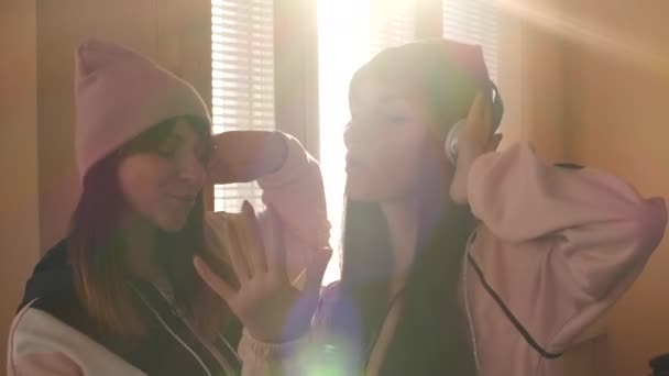 Dos hermanas activas en sombreros y auriculares escuchando música — Vídeos de Stock