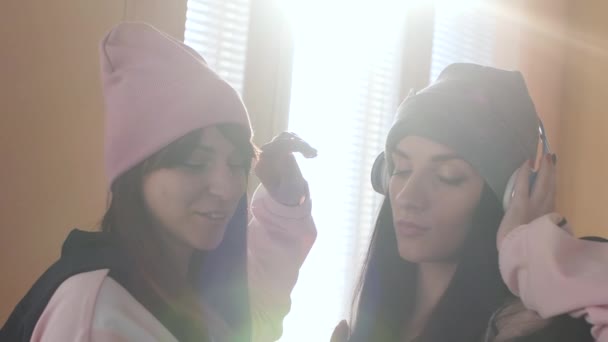 Dos hermanas activas en sombreros y auriculares escuchando música — Vídeo de stock