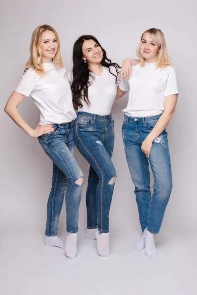 Tres hermosas mujeres en camisas blancas y jeans posando — Foto de Stock