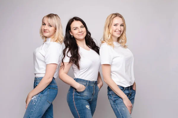 Tres hermosas mujeres en camisas blancas y jeans posando — Foto de Stock