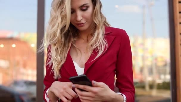 Elegante rubia en traje rojo inteligente usando teléfono y mensajería — Vídeos de Stock
