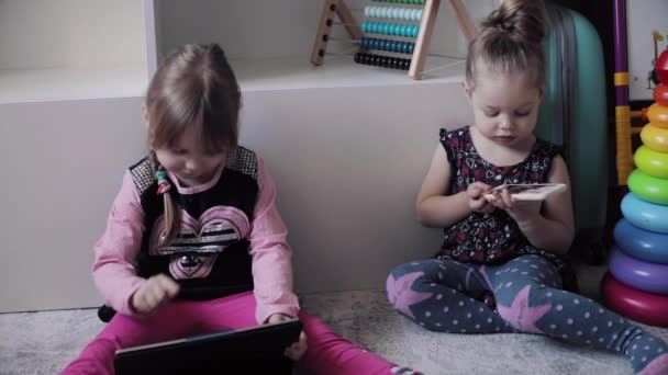 Hauska lapsi istuu lattialla ja käyttää elektronisia laitteita . — kuvapankkivideo