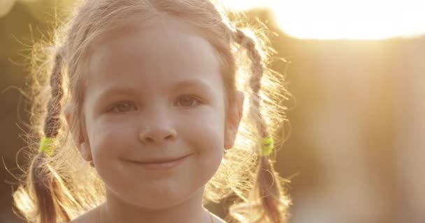 Preciosa niña sonriendo a la cámara a la luz del sol retroiluminada . — Vídeos de Stock