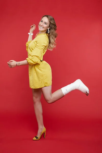 그녀의 다리에 석고와 함께 재미를 노란색 드레스에 쾌활한 아름다운 여자. — 스톡 사진