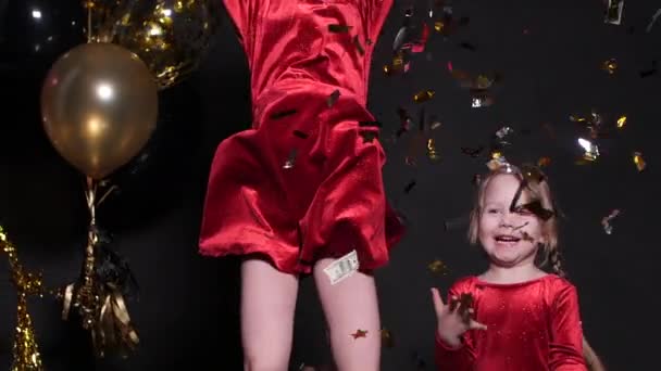 Preciosa niña feliz saltando con confeti y globos de aire en el fondo . — Vídeo de stock