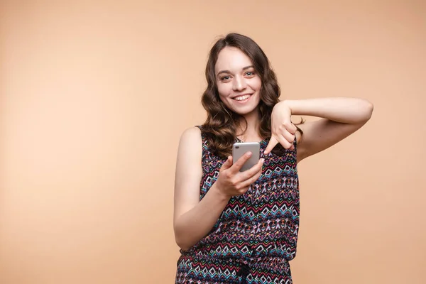 Pretty girl pointing at cell phone.Studio portrait of beautiful caucasian — Stock Photo, Image