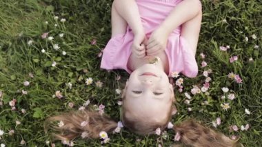 Yakın çekim gülümseyen küçük sevimli bebek kız yeşil çim enelinde yatan çiçekler kameraya bakarak