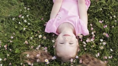 Yakın çekim gülümseyen küçük sevimli bebek kız yeşil çim enelinde yatan çiçekler kameraya bakarak