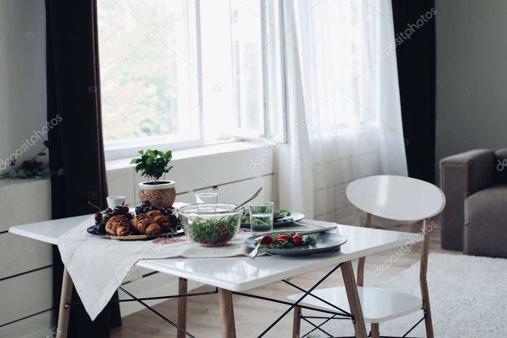 Table with healthy tasty breakfast surrounded by modern interior at summer morning