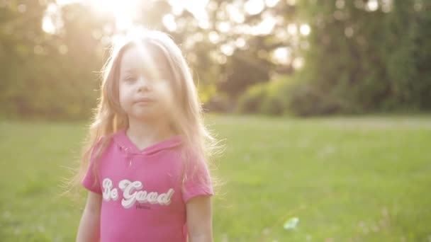 Vitryssland Minsk 05 25 2019: söt liten flicka med ponny svansar plocka Blommor kronblad på ängen. — Stockvideo