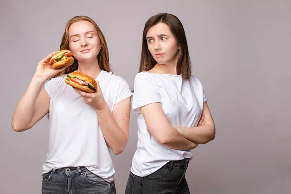 Dwie frown Młoda piękna kobieta trzyma apetyczny Burger patrząc na kamerę — Zdjęcie stockowe