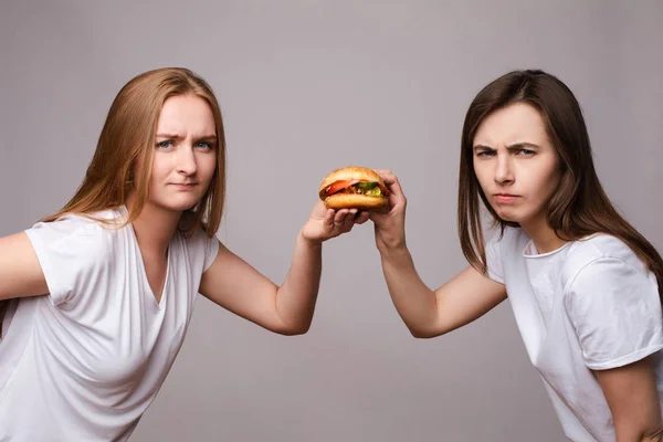 Дві молода красива жінка тримає апетитний шкідливий бургер, дивлячись на камеру — стокове фото