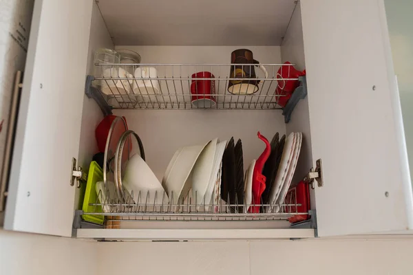 Чистые блюда в сушильном шкафу. Открытая дверь кухонного шкафа с чашками, кружками и мисками и тарелками для сушки на полках . — стоковое фото