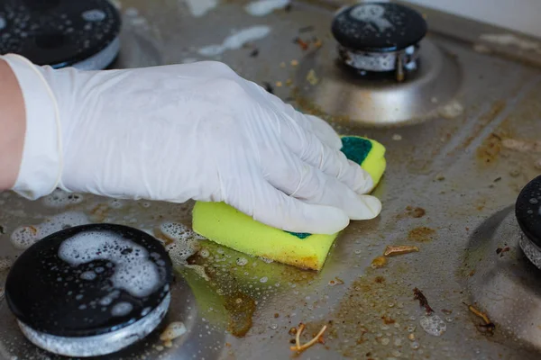 Domestic female hand wearing gloves cleaning dirty stove after cooking using sponge for washing — Stock Photo, Image