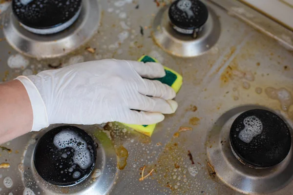 Бытовая женская рука в перчатках для чистки грязной печи после приготовления пищи с использованием губки для стирки — стоковое фото