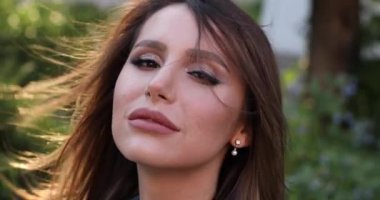 Sokakta yürürken kameraya gülümseyen esmer saçlı mutlu güzel kadın.