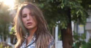 Sokakta yürürken kameraya gülümseyen esmer saçlı mutlu güzel kadın.