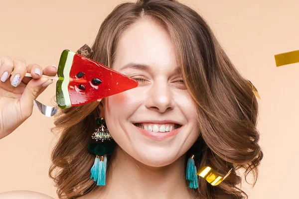 Playful young elegant smiling woman posing with piece watermelon candy at studio background