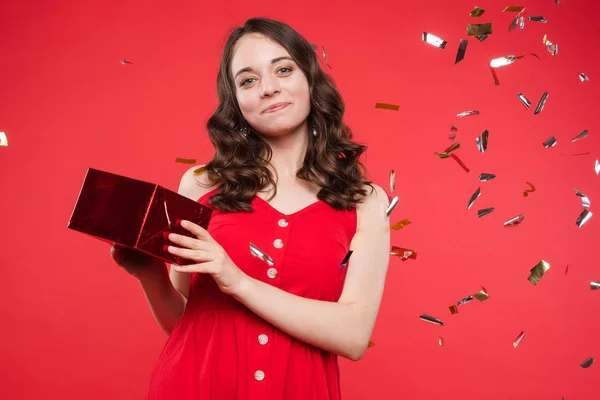 Portrait of adorable smiling young woman with long curly hair posing at red studio background