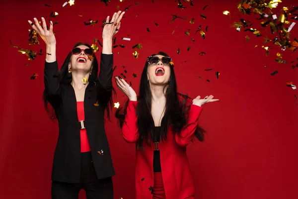 Zwei junge Mode stilvolle weibliche Modell mit Sonnenbrille lächelnd posiert isoliert im roten Studio — Stockfoto