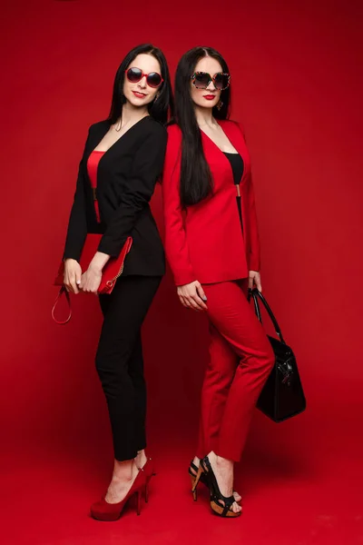 Twee jonge mode stijlvolle vrouwelijke model in zonnebril glimlachend poseren geïsoleerd bij Red Studio — Stockfoto