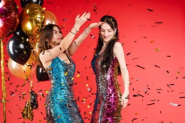 Grup gülümseyen kadın renkli parıldayan konfeti izole kırmızı stüdyo arka plan ile çevrili poz
