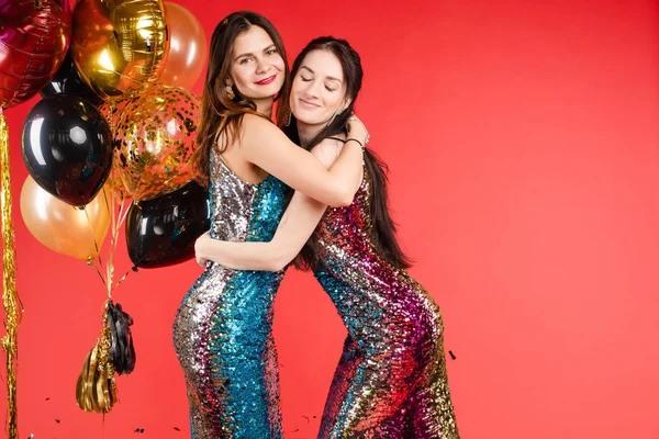 Grupo sonriente mujer posando rodeado de colorido confeti brillante aislado fondo de estudio rojo — Foto de Stock