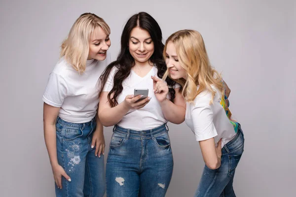 Chicas mirando la pantalla del teléfono juntos.Retrato de estudio de dos chicas mirando el teléfono móvil mientras las chicas rubias lo usan. Concepto de chismes o rumores. Aislar . — Foto de Stock