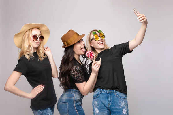 Amiga sonriente que usa un divertido sombrero de máscara y anteojos posando tomando selfie usando un teléfono inteligente — Foto de Stock