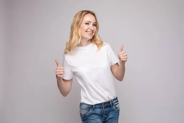 Positiv blondin i vit skjorta och jeans som visar tummen upp — Stockfoto