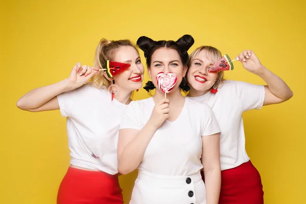 Gruppo bella ragazza amica rilassante insieme in posa con dolci caramelle colorate a studio giallo — Foto Stock