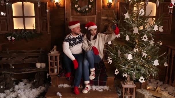 Feliz pareja en invierno sombreros y mitones toma selfie a través de móvil . — Vídeo de stock