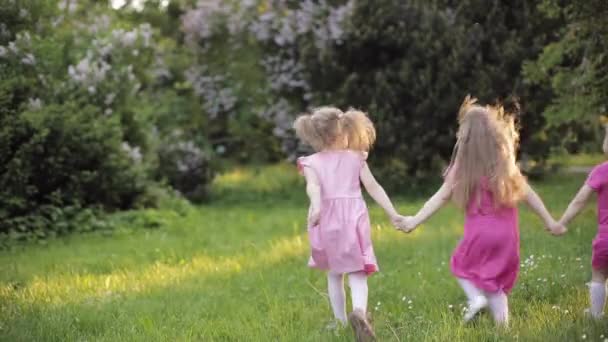 Trzy małe dziewczynki trzymającej przez ręce działa na zielonej trawie w ogrodzie otoczonym dmuchawą bąbelkową powietrza — Wideo stockowe